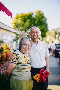 An elderly couple stands at a flower stand on a summer day.