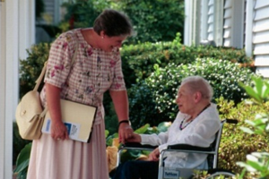 a home care aide assists a patient in a wheelchair at their home