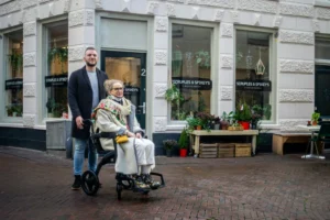 Caregiver pushing woman in wheelchair outside shop front