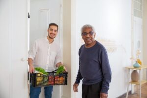 A home health aide delivers a box of fresh fruit and vegetables to a senior client.