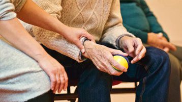 The nurse is helping the man holding an exercise ball.