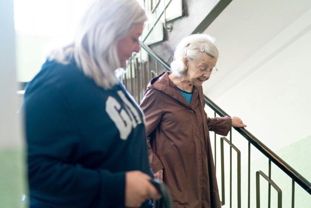 A Caregiver helps an elderly woman down the stairs.