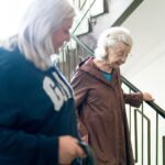A Caregiver helps an elderly woman down the stairs.