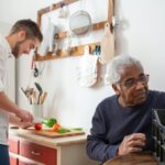 A live-in caregiver prepares a meal as he chats with a senior man