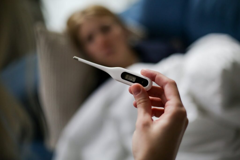 A hand holding a thermometer reading the temperature of an elderly with the flu